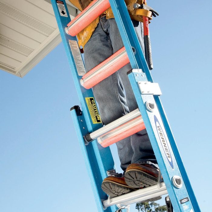 a man standing on a ladder with pink pool noodles on each rung of the ladder